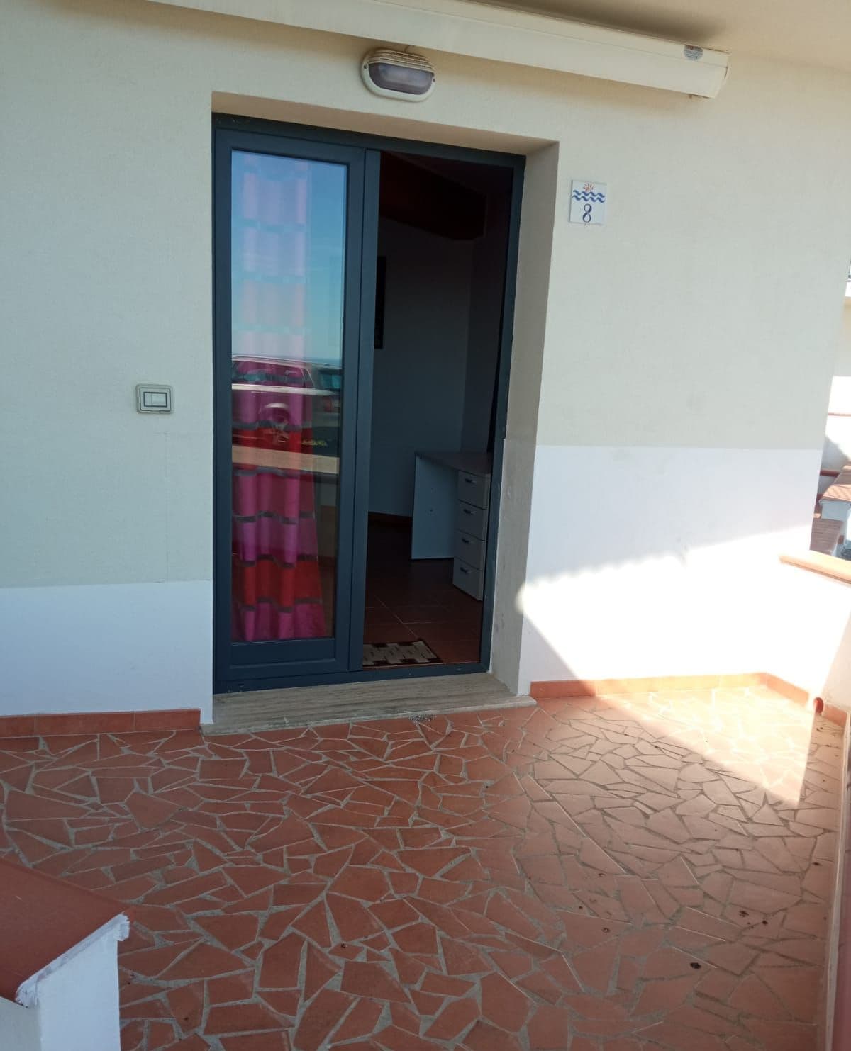 Ein Gebäudeeingang mit einer gefliesten Terrasse, einer Schiebeglastür und einem kleinen Schild mit der Nummer 8.