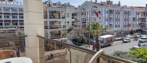 Un balcón con una mesa y sillas, con vista a una calle con edificios y un camión estacionado.