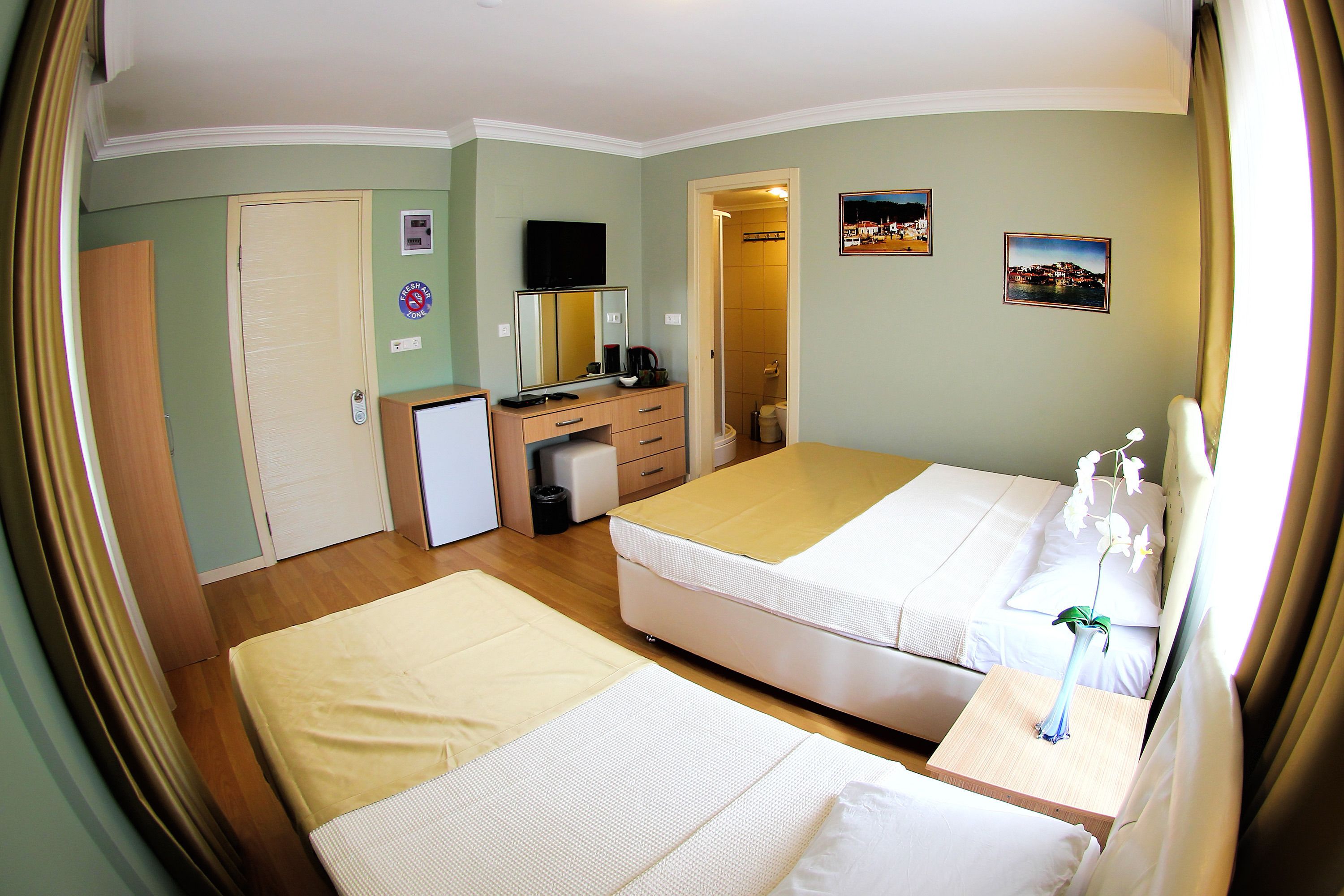 A hotel room with two beds, a desk with a computer, a small bathroom, and a door leading to another room.