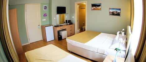 Habitación de hotel con dos camas, un escritorio con computadora, un baño pequeño y una puerta que da a otra habitación.
