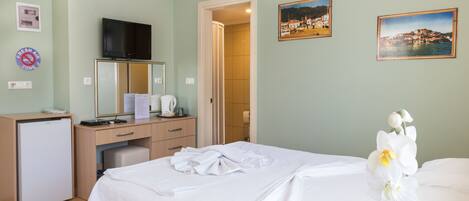 Una habitación de hotel con una cama, un escritorio con televisor, un refrigerador y dos cuadros en la pared.