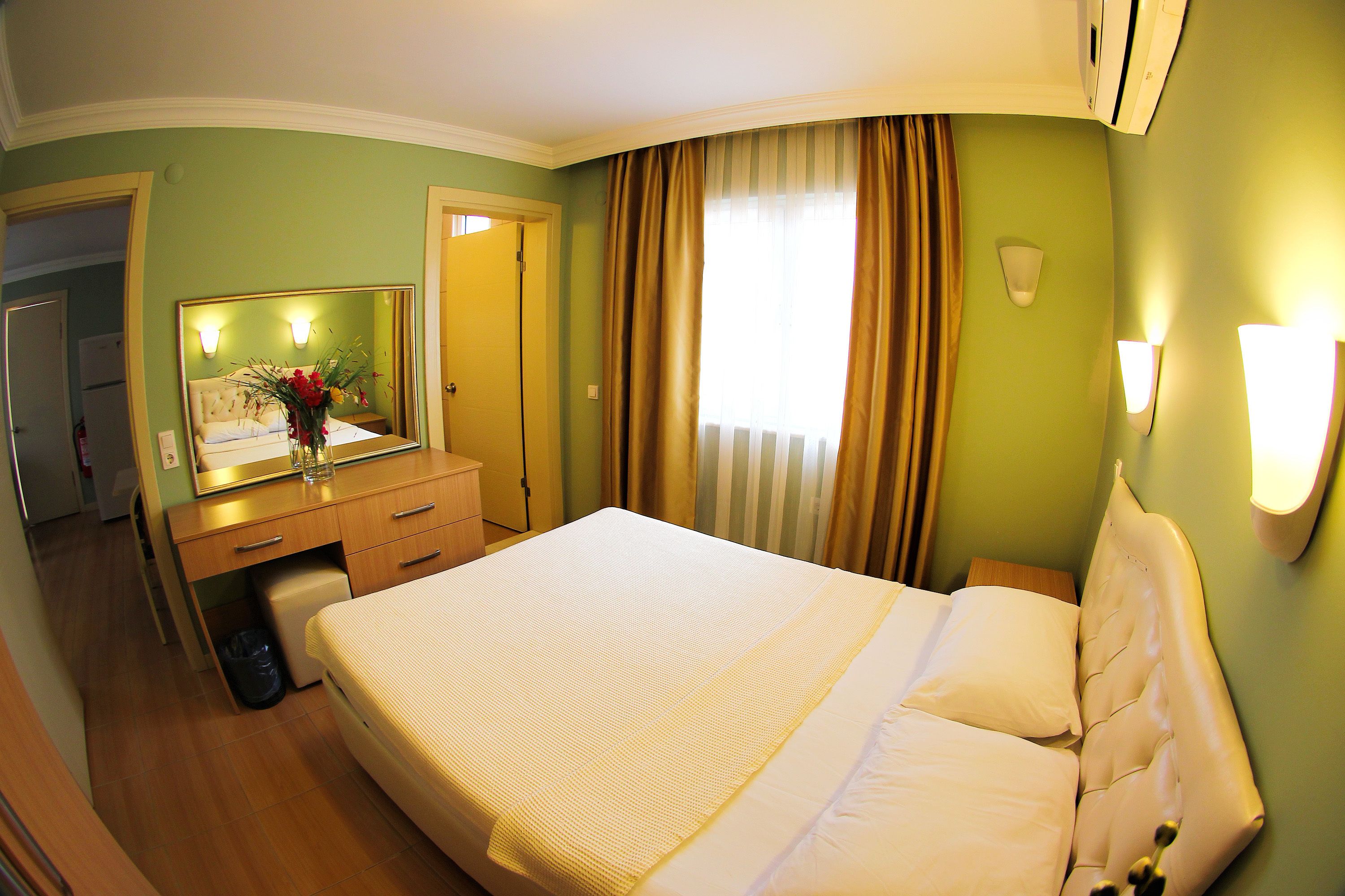Habitación de hotel con una cama grande, un tocador con espejo, un escritorio pequeño y una ventana con cortinas.