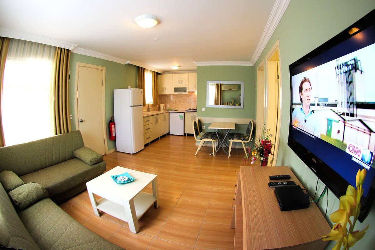 A living room with a sofa, coffee table, TV, and a dining area with chairs and a table.