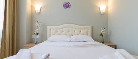 A neatly made bed with white linens and pillows, two bedside tables with lamps, and a wall-mounted sign indicating a fresh air zone.