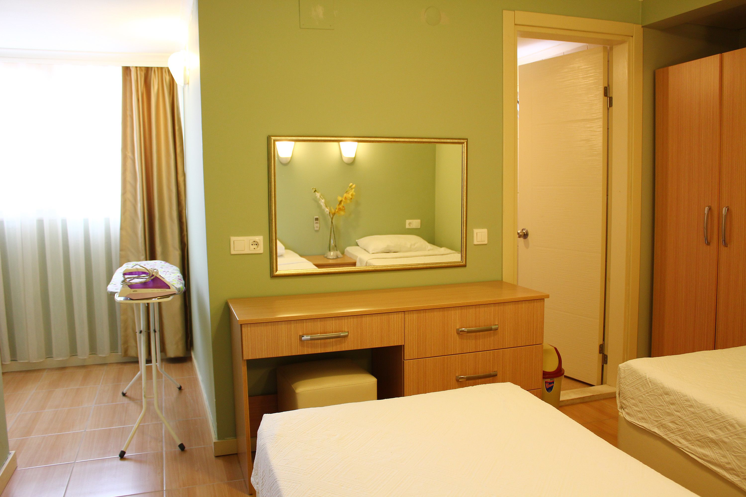 A hotel room with a bed, a dresser, a mirror, and a window with curtains.