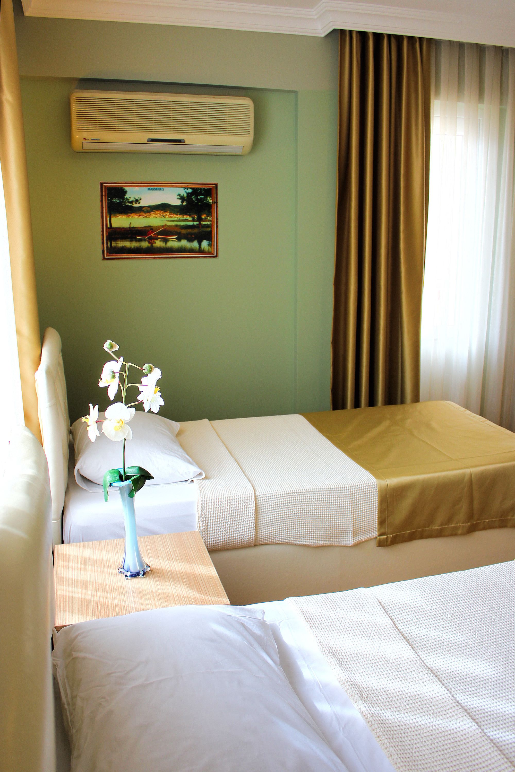 A hotel room with two beds, a painting on the wall, and a window with curtains.