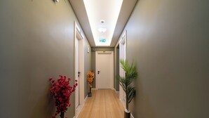 Un couloir avec un plancher en bois, une porte au fond et une plante sur la droite.