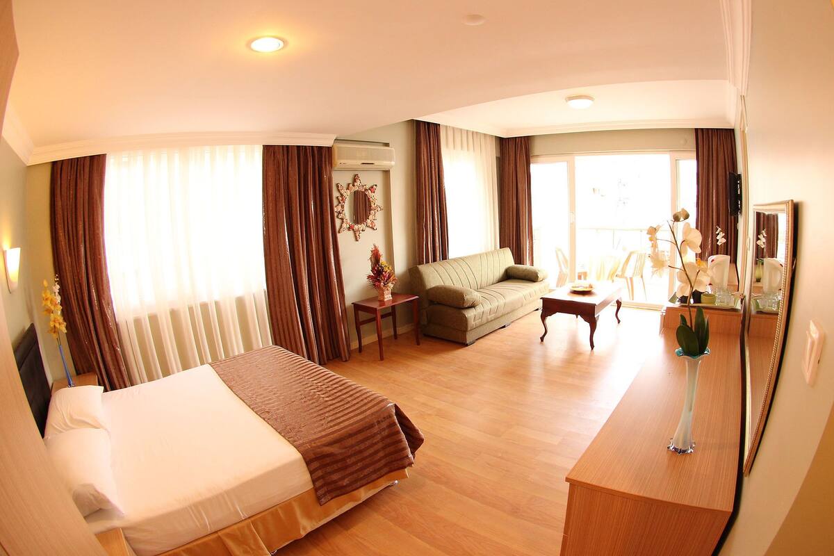A hotel room with a bed, a sofa, a small table, and a mirror.