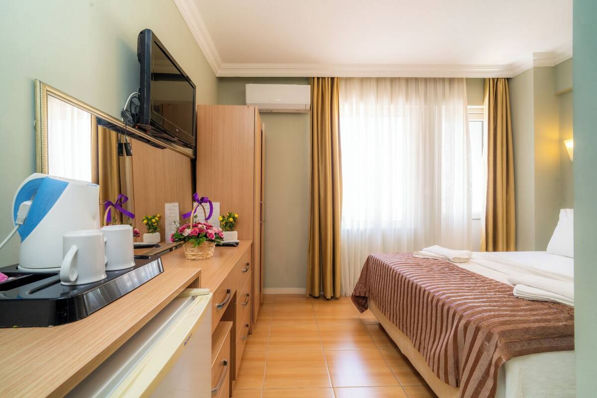 A hotel room with a bed, a desk with a computer, a microwave, a coffee maker, and a small table with flowers.