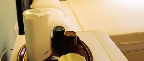 Une chambre d’hôtel avec un lit, une table de chevet sur laquelle se trouve un plateau contenant une machine à café, une tasse, ainsi qu’un salier et un poivrier.