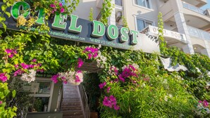L’entrée d’un hôtel, agrémentée d’une enseigne indiquant « EL DOST », est entourée d’une végétation luxuriante et de fleurs.