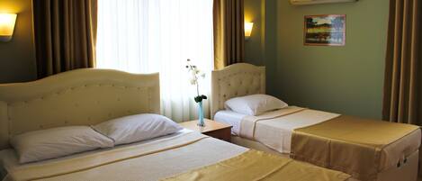 A hotel room with two beds, a nightstand, a vase with flowers, and a painting on the wall.