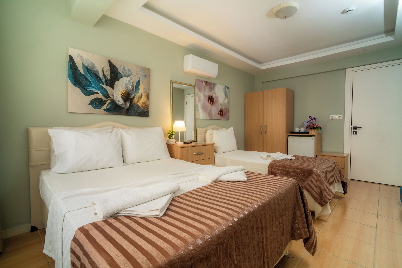 A hotel room with two beds, a wardrobe, a desk with a lamp, and a mirror.