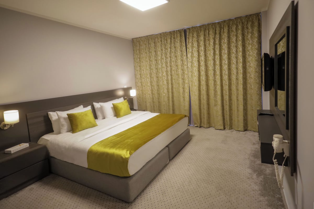 Una habitación de hotel con una cama grande, una mesita de noche, un televisor y una cortina.
