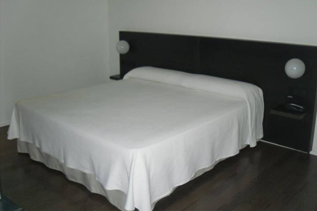 A neatly made bed in a room with a dark headboard and a small bedside table with a lamp.