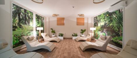 A room with four beige lounge chairs arranged in a semi-circle, a wooden floor, and large windows with tropical wallpaper.