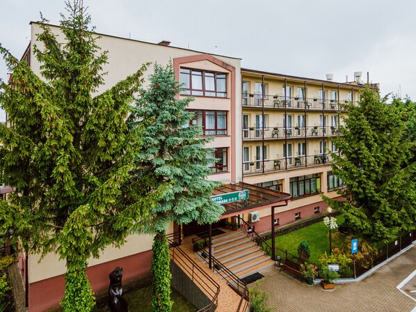 Un hotel de varios pisos con una escalera central, balcones en cada planta y un pequeño patio con vegetación.