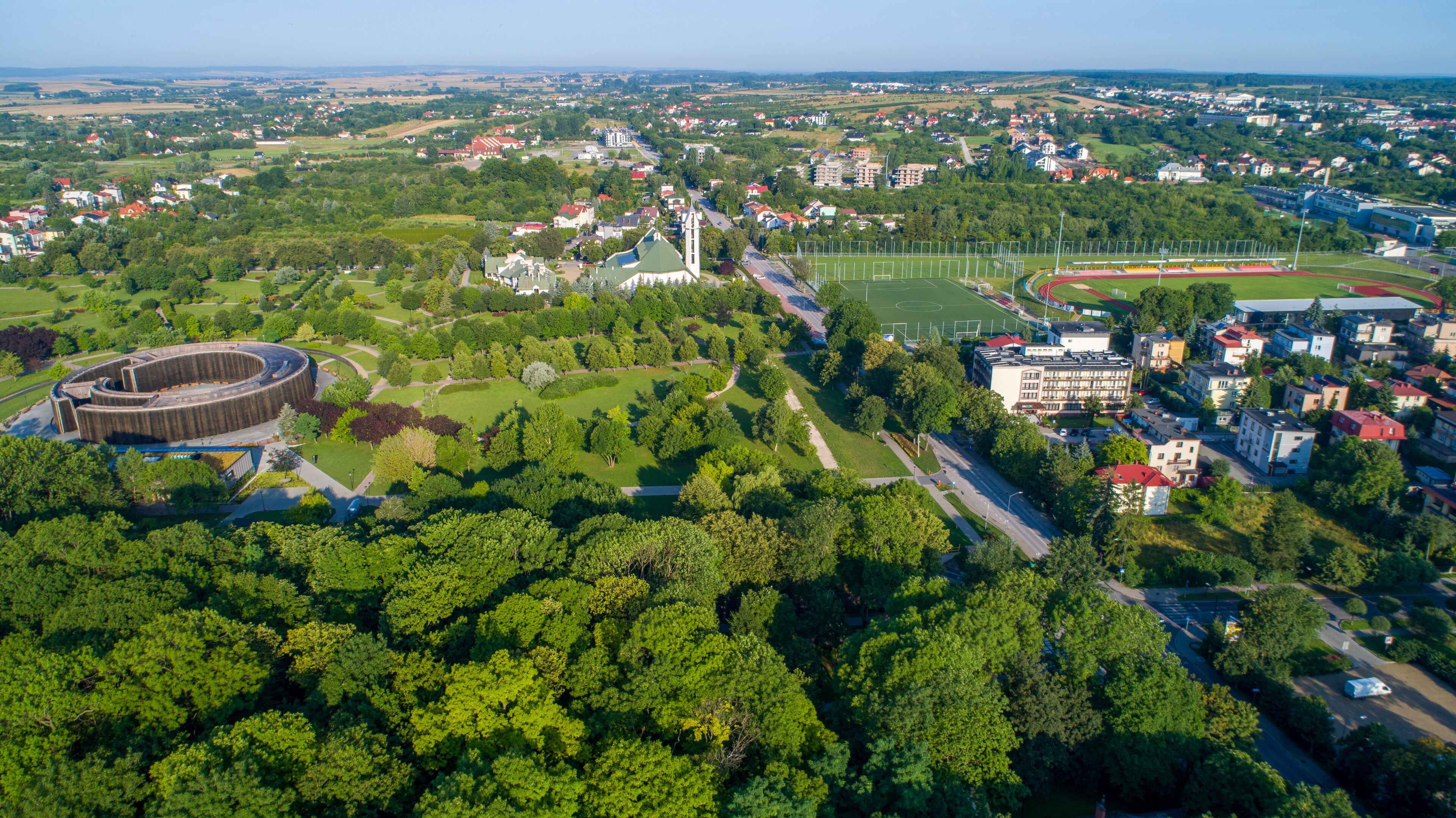 An aerial view of a town with a large stadium, a church, and residential buildings.