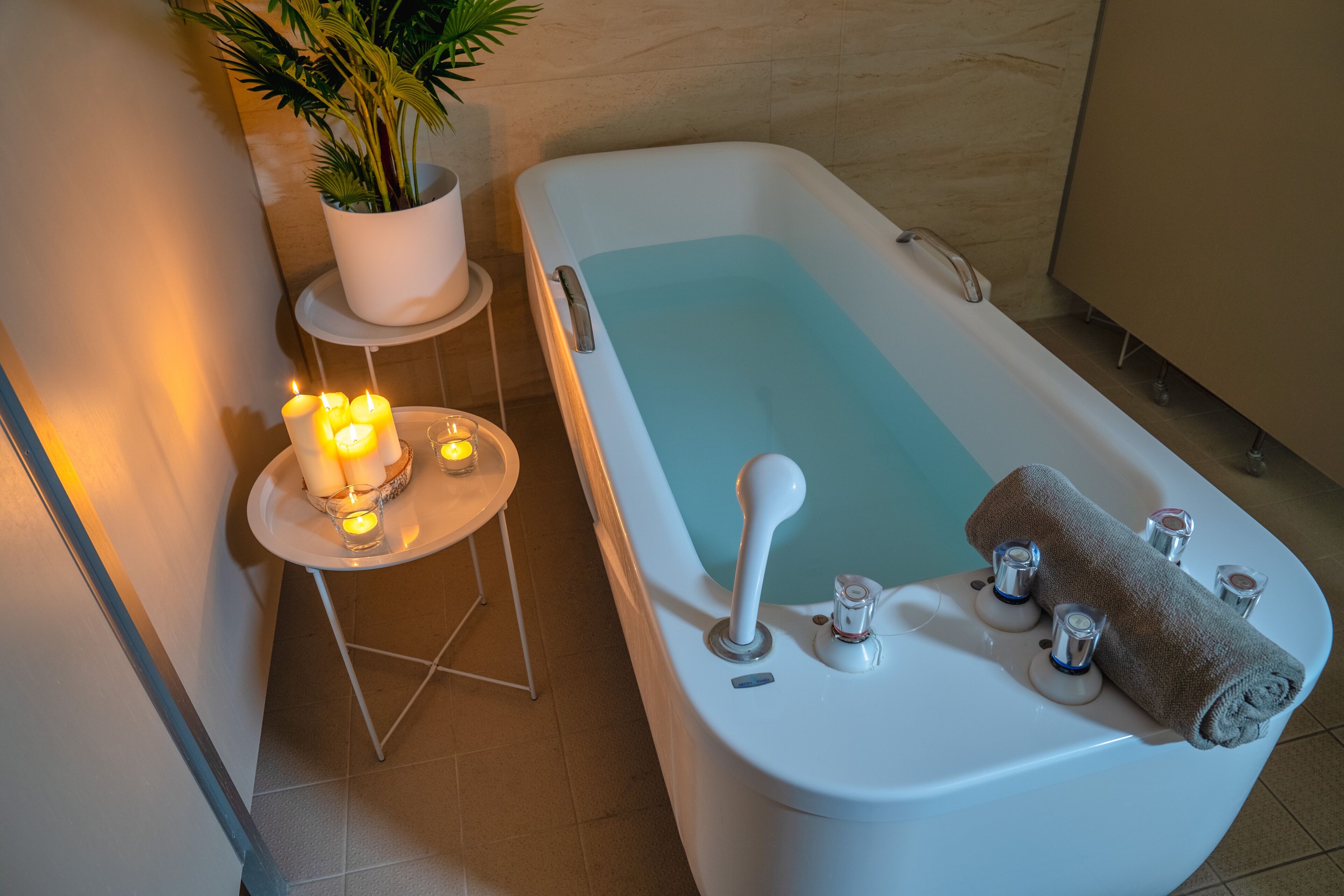 A bathroom with a bathtub, a small table with candles, and a potted plant.