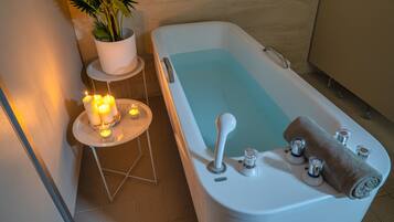 A bathroom with a bathtub, a small table with candles, and a potted plant.