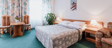 A hotel room with a bed, a desk, a chair, a table, and a plant.