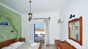 A hotel room with a bed, a desk, a chair, a mirror, and a view of the outdoors. - Hotel Olympia (Santorini)