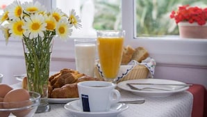 A breakfast table with a vase of daisies, a glass of orange juice, croissants, and a cup of coffee. - Hotel Olympia (Santorini)