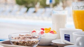 A breakfast setting with a bowl of granola, a fruit salad, a glass of milk, and a glass of orange juice on a tray. - Hotel Olympia (Santorini)
