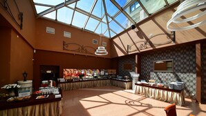 A spacious room with a high ceiling and skylight, featuring a buffet setup with various food items and a seating area with a table and chairs. - Hotel Gromada Pila (Pila)