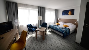 A hotel room with a bed, a desk with a TV, a chair, a table, and a window with curtains. - Hotel Gromada Pila (Pila)