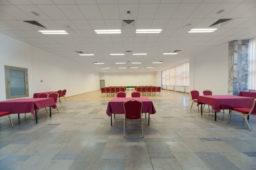 Una sala de conferències amb diverses taules i cadires, un sòl de rajoles i una finestra gran a un costat.