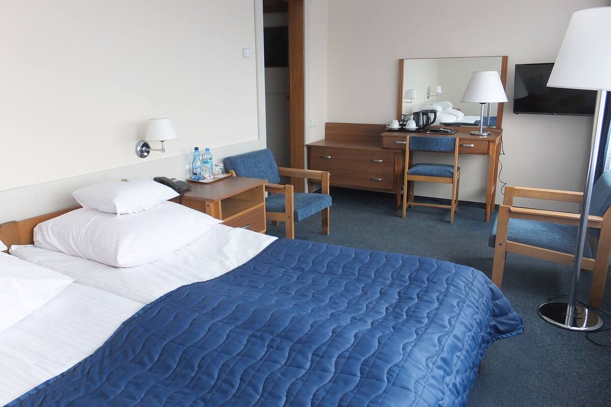 A hotel room with a bed, desk, chair, and a TV.