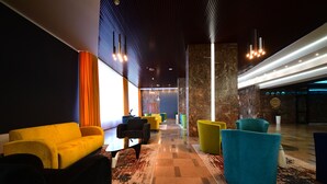 A modern lobby with vibrant yellow and teal seating, a patterned carpet, and a stone accent wall. - Hotel Gromada Pila (Pila)