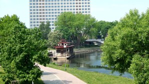 A riverside walkway with a boat dock, surrounded by lush greenery and a large building in the background. - Hotel Gromada Pila (Pila)