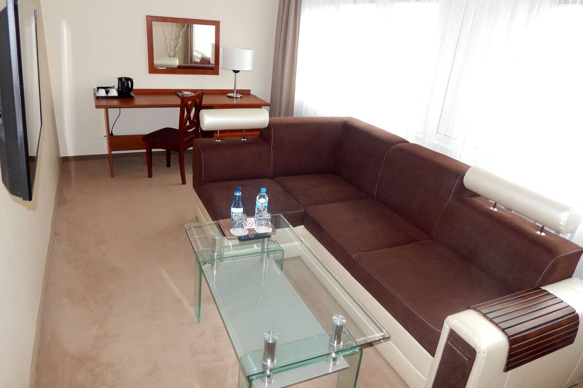 A living room with a brown leather sofa, a glass coffee table, a wooden desk, and a television.