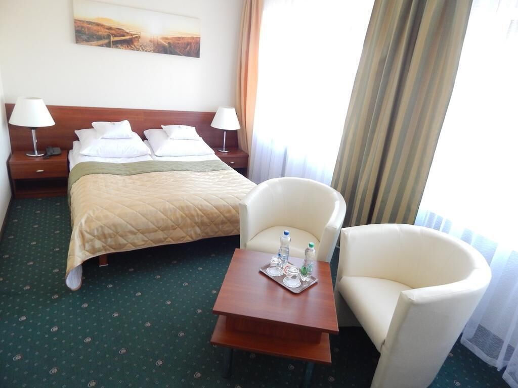 Ein Hotelzimmer mit einem Bett, zwei Nachttischen, einem Sessel, einem kleinen Tisch mit Tablett und einem Bild an der Wand.