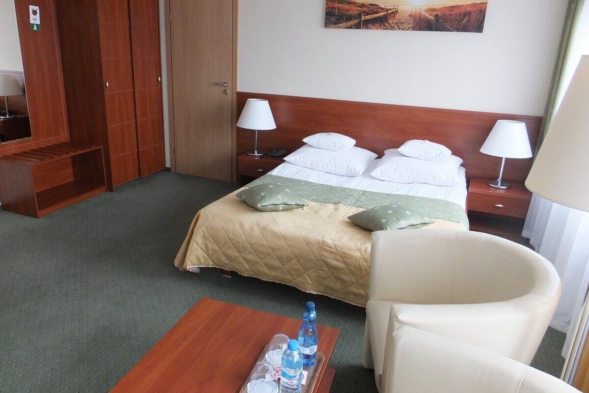 A hotel room with a bed, two bedside tables, a chair, a wooden desk, and a wardrobe.