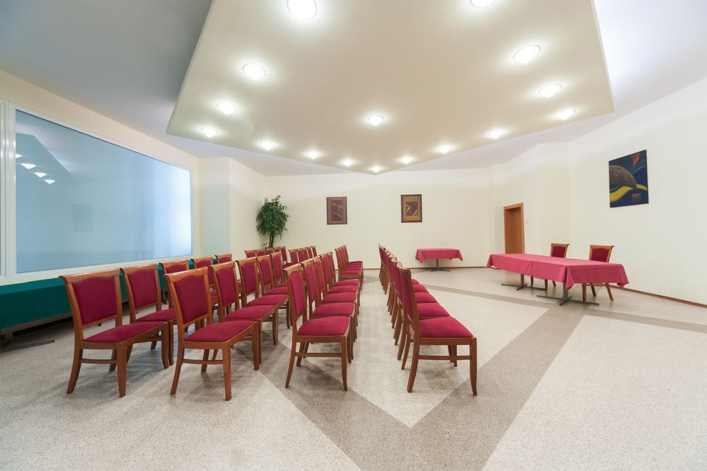 Une salle de conférence avec des rangées de chaises et de tables en bois, un grand écran de projection et des luminaires au plafond.