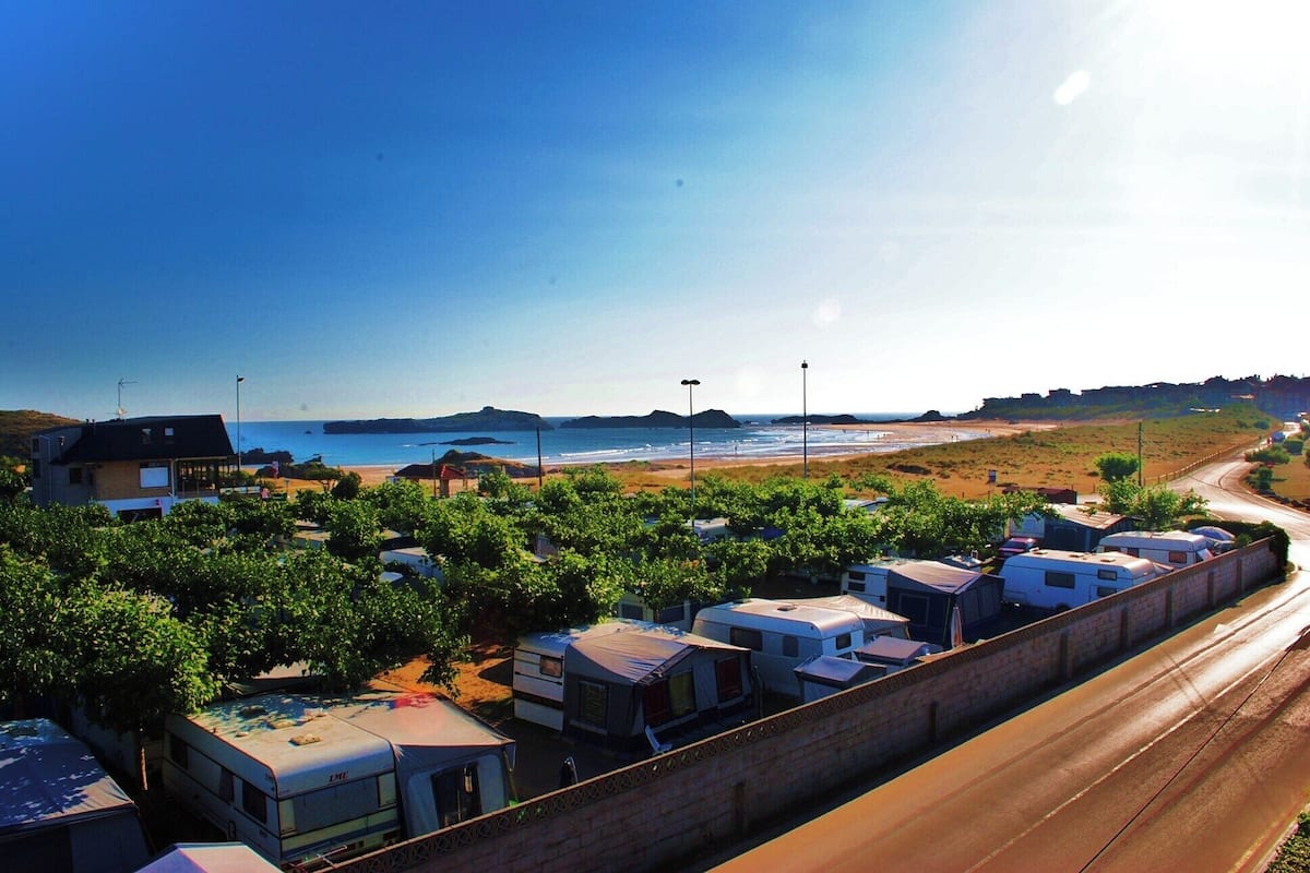 A caravan park with multiple caravans parked in rows, a beach in the background, and a clear sky.