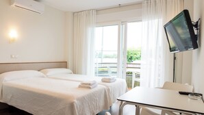 Habitación de hotel con dos camas, televisión, mesa y balcón con cortinas.