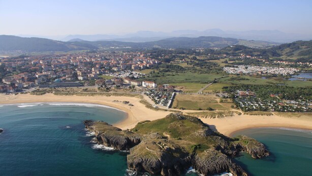 Vista aérea de un pueblo costero con playa, afloramientos rocosos y zonas residenciales.