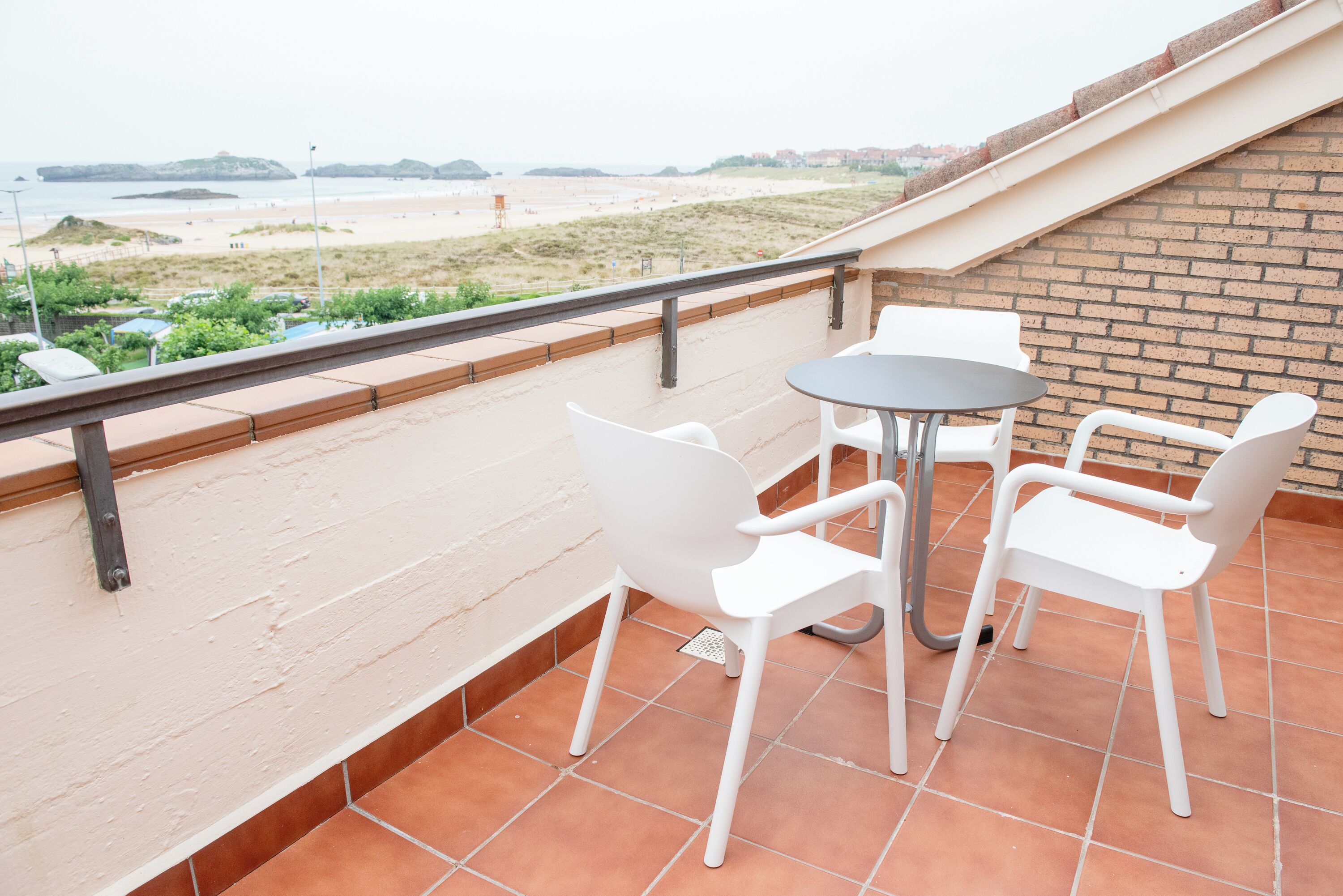 A terrace with a table and chairs, overlooking a beach and a distant cityscape.