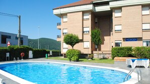 Una piscina con sillas de descanso, un edificio de ladrillo con balcones y un letrero que dice 'APARTMENTS'.