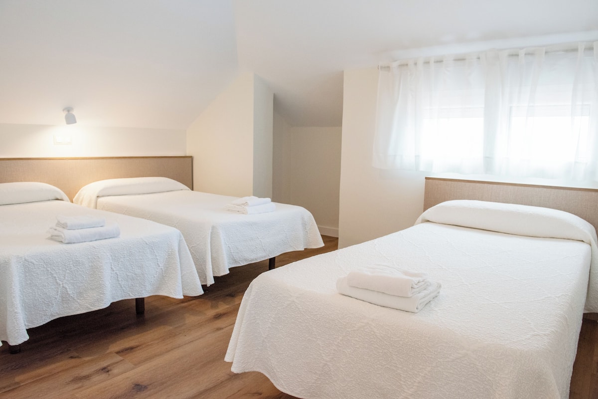 A hotel room with two single beds, each with a white bedspread and a folded towel. The room has wooden flooring and a large window with sheer curtains.
