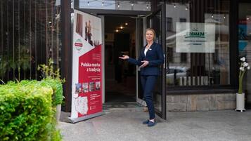 Een vrouw staat bij de ingang van een hotel, met een bord waarop Poolse tradities worden aangekondigd.