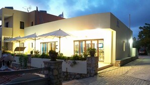 A modern two-story building with outdoor seating and a stone pathway leading to the entrance. - Miraluna Hotel (Karpathos)