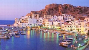 A coastal town with a marina filled with boats, buildings with balconies overlooking the water, and a rocky hill in the background. - Miraluna Hotel (Karpathos)