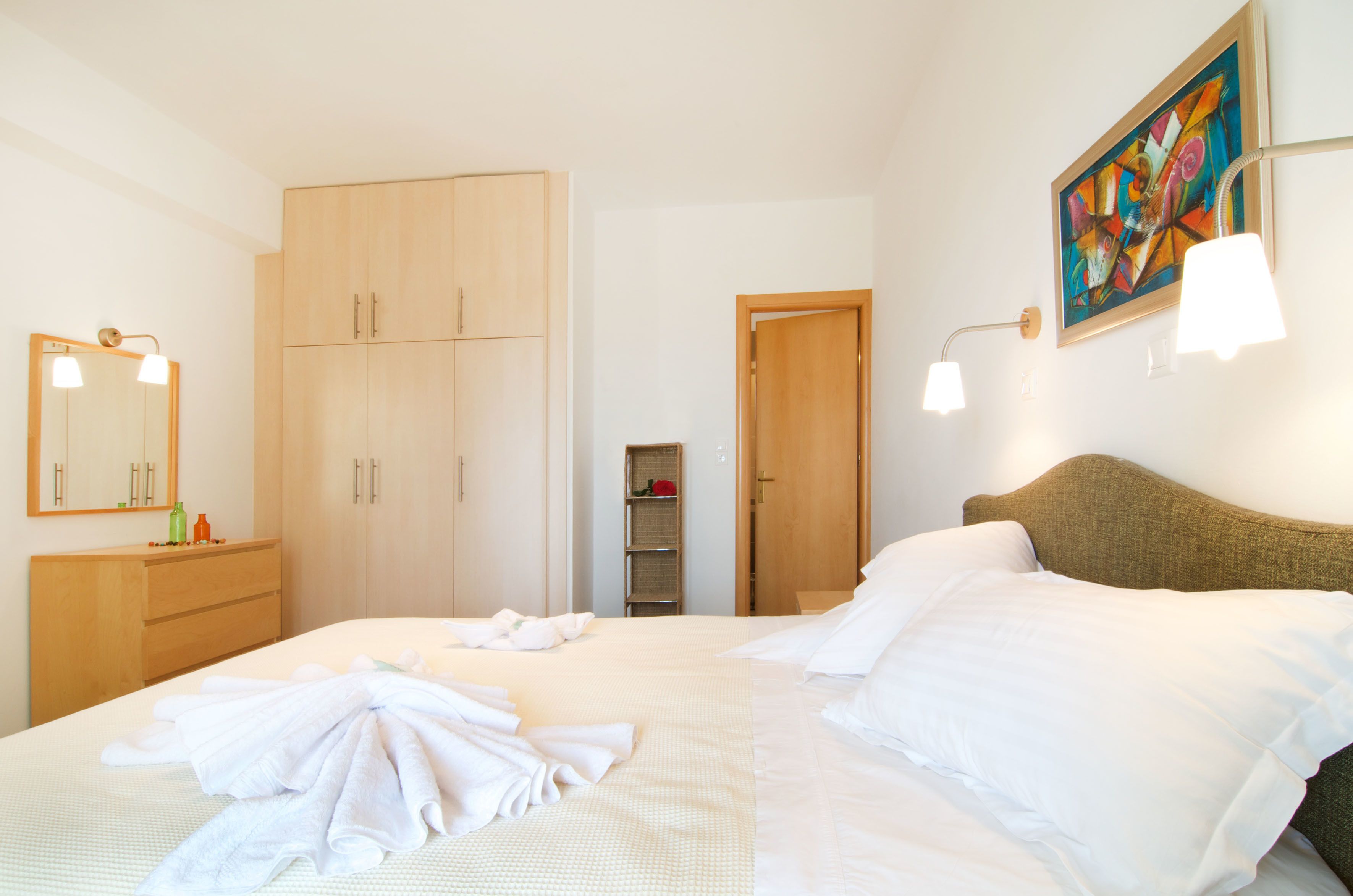 A hotel room with a bed, a wardrobe, a bathroom, and a painting on the wall.