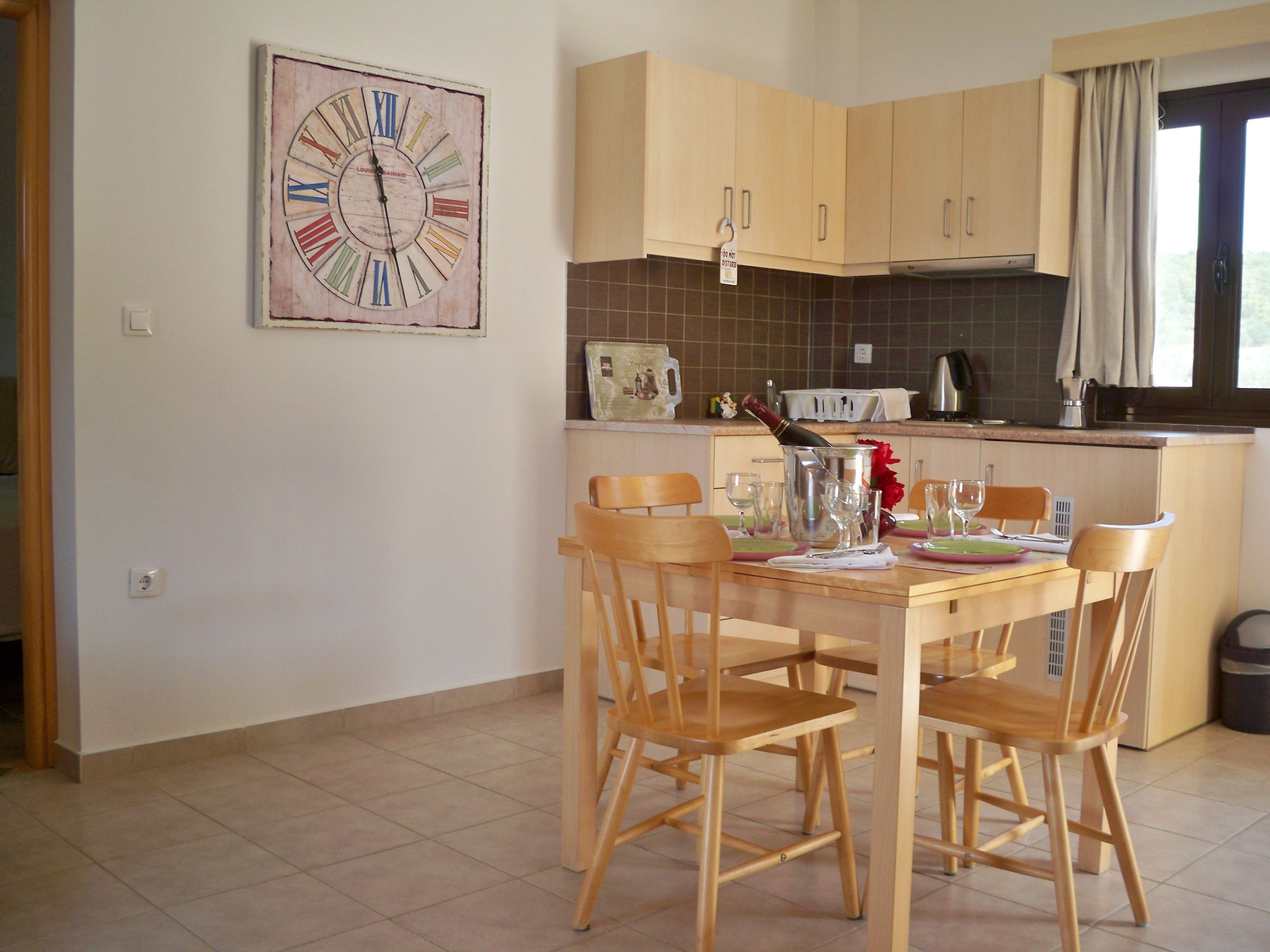A kitchen with wooden cabinets, a dining table with chairs, a clock on the wall, and a bottle of champagne.