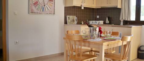 A kitchen with wooden cabinets, a dining table with chairs, a clock on the wall, and a bottle of champagne.